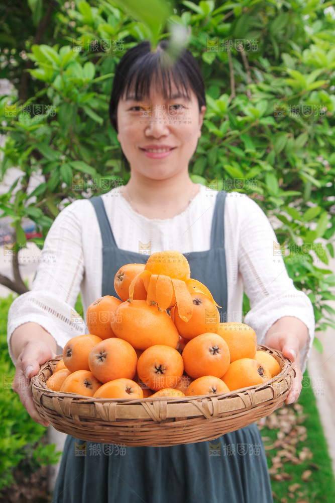 女人手里端着一篮枇杷