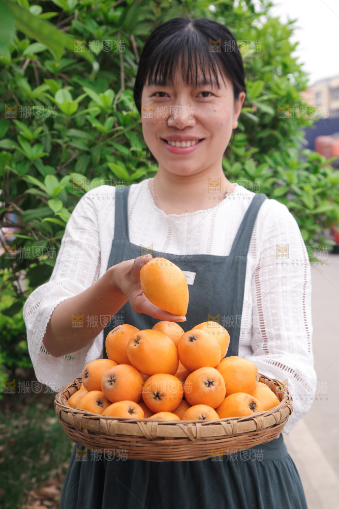 女人手里端着一篮枇杷